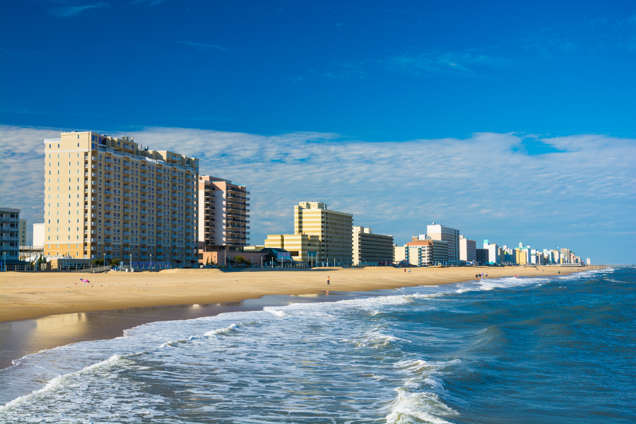 Wide sandy beach with gentle waves, lined with tall beachfront buildings under a clear blue sky. Few travelers can be seen strolling on the shore. A long coastline stretches into the distance, offering a serene escape for those seeking peace and relaxation.